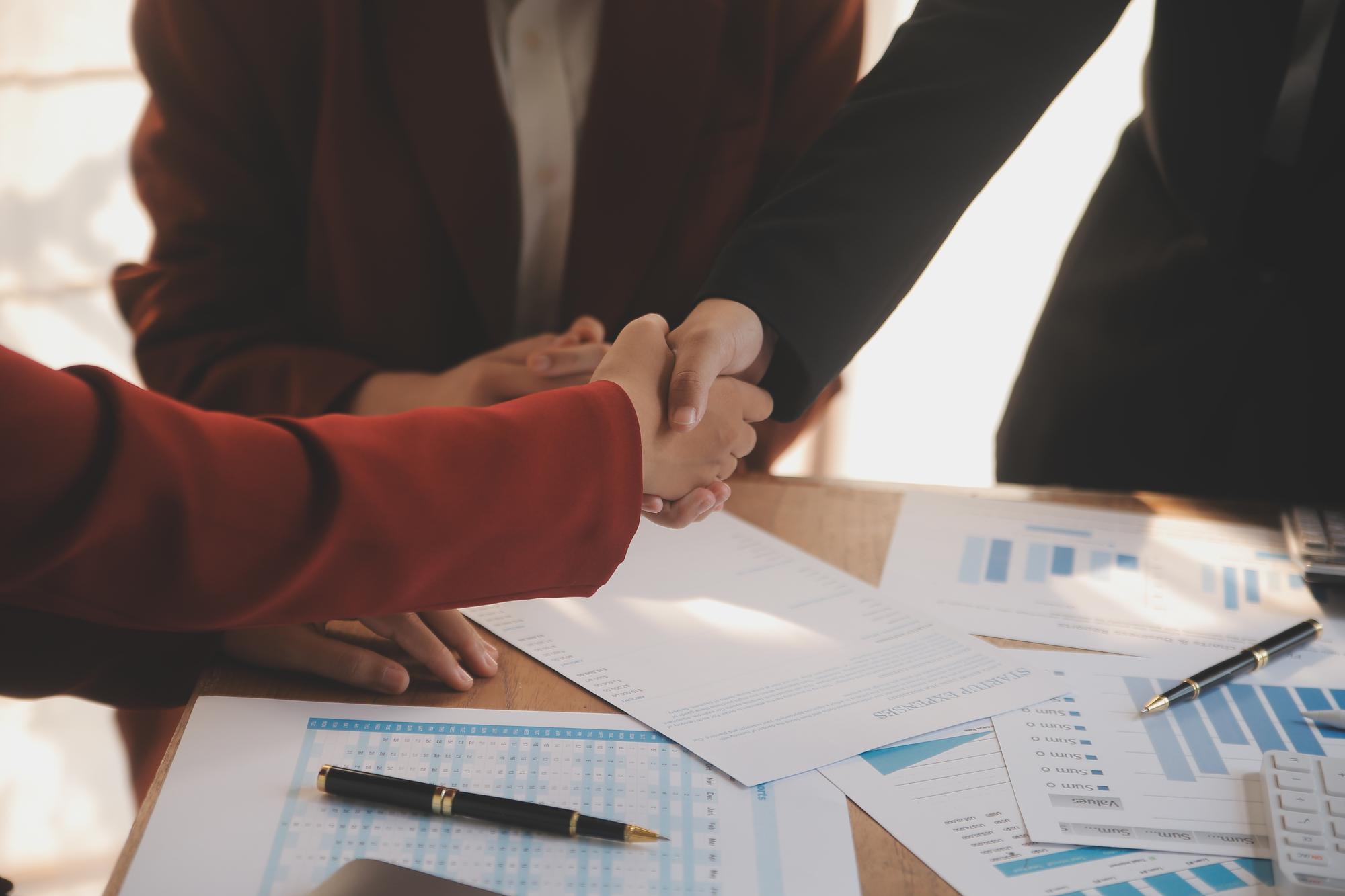 Nahaufnahme von Finanzdokumenten und Handschlag